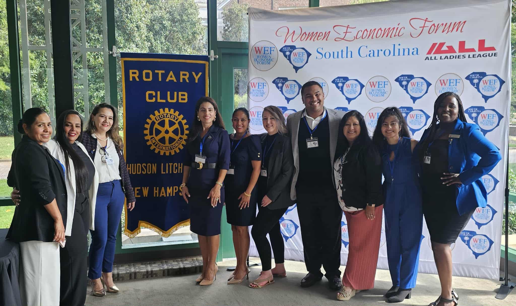 Group of nine women standing in front of banners at an event, smiling and posing for the photo.