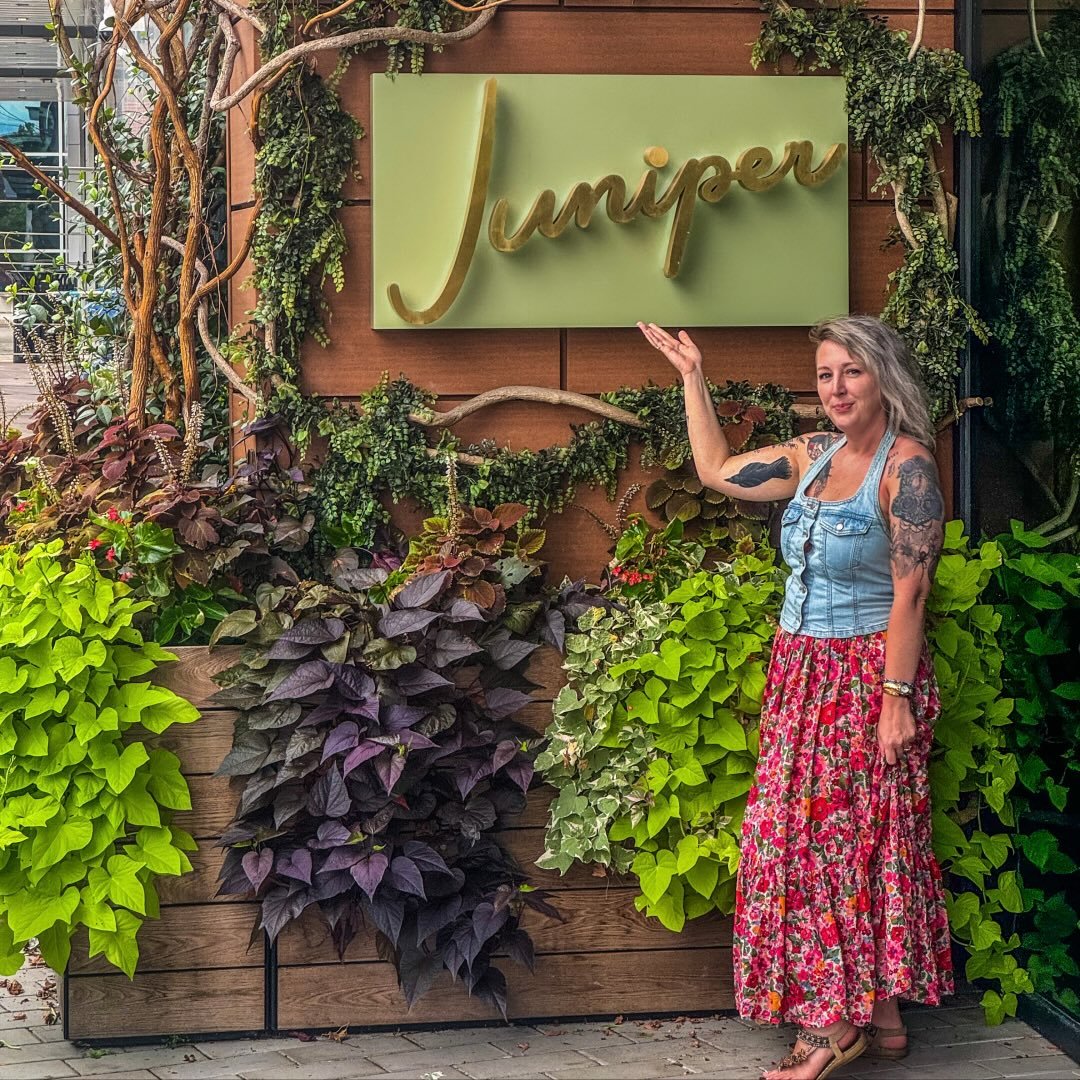 Woman with tattoos and long hair standing next to a green sign that says 