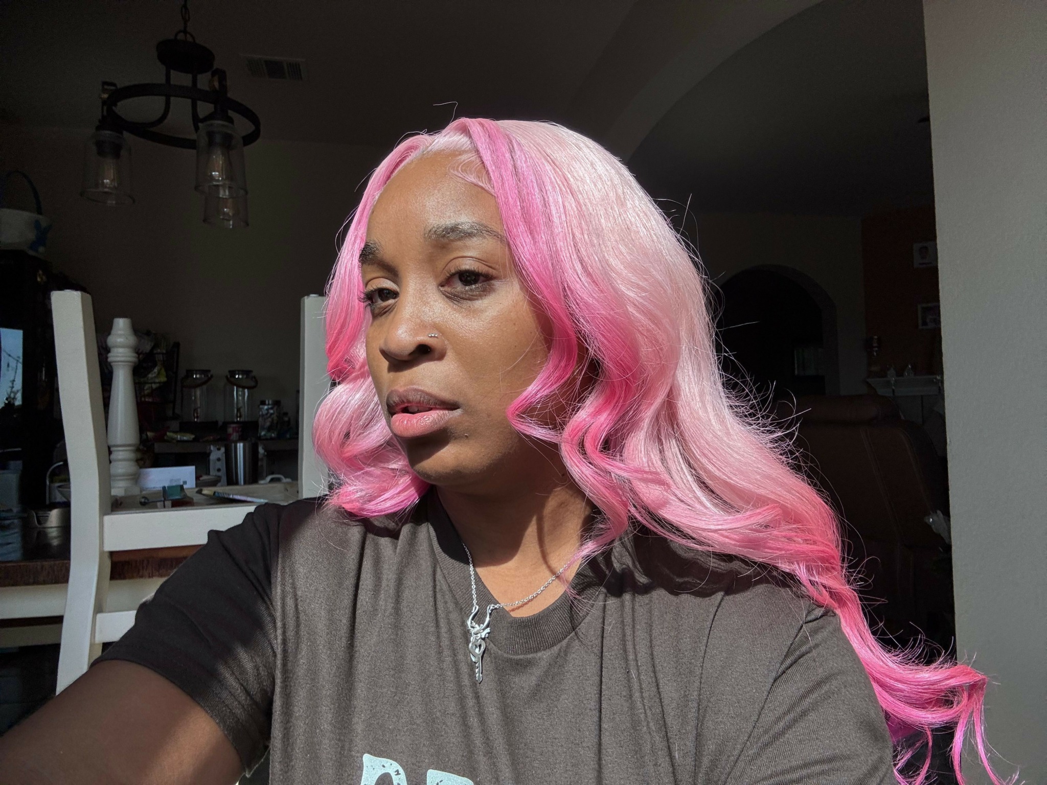 Person with pink and white hair lying on a chair in a room with furniture and a chandelier.