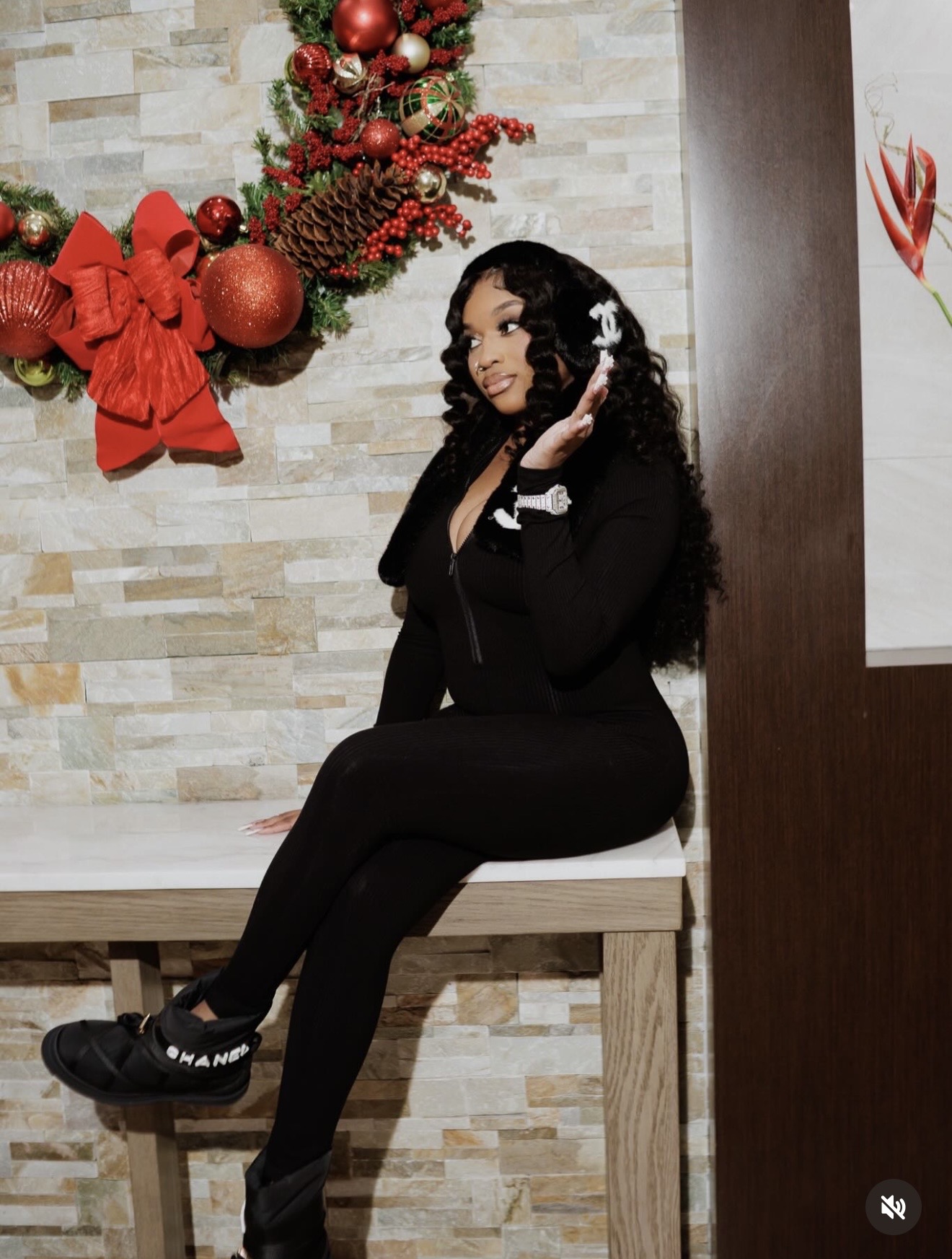 Woman sitting on a bench with Christmas decorations behind her, wearing black clothing and headphones, smiling.