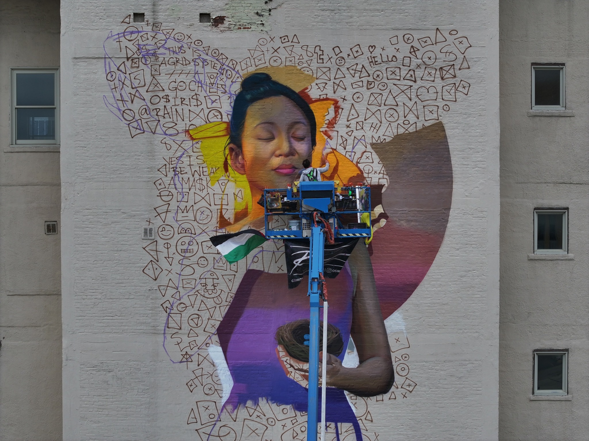 Mural of a woman with closed eyes, holding a ball, surrounded by colorful abstract shapes and patterns on a building wall.