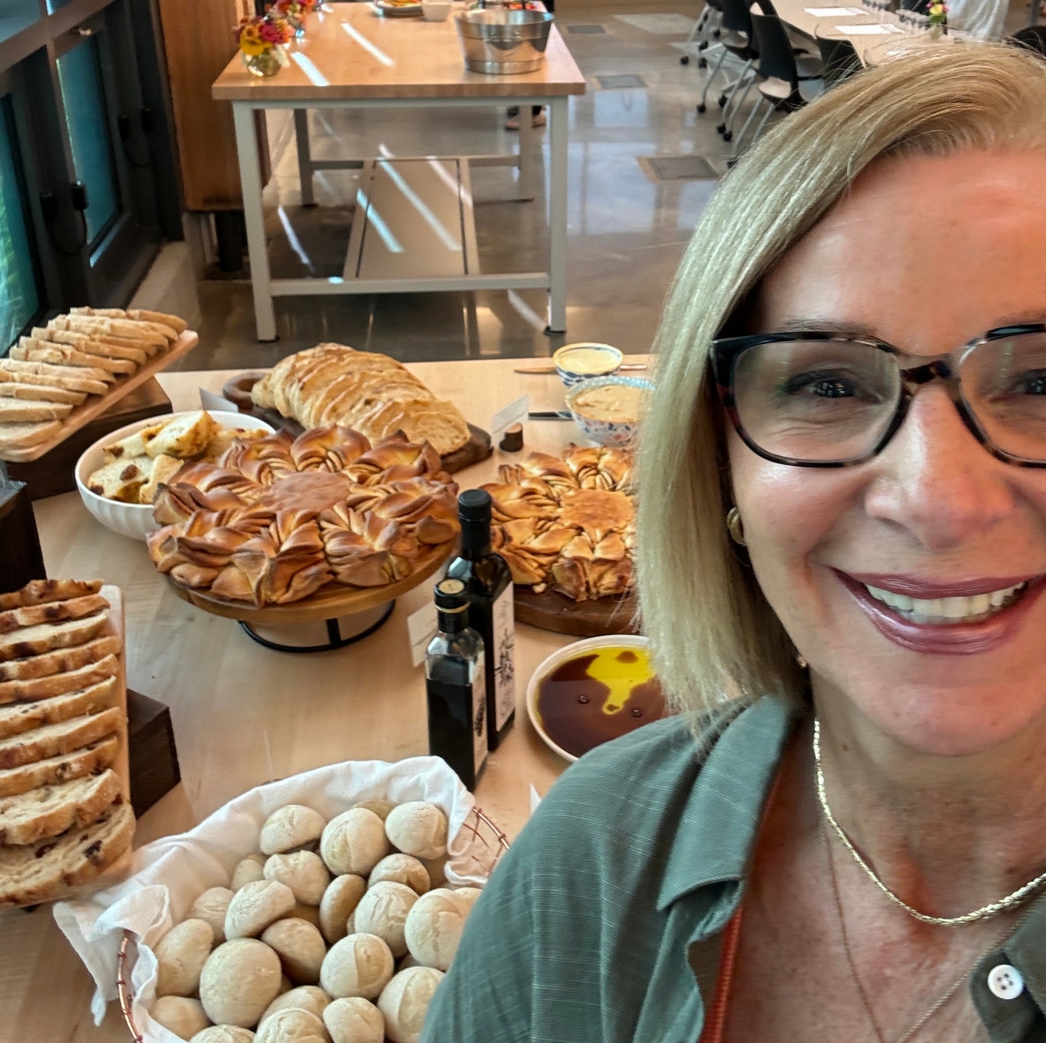 Smiling woman with glasses in front of a table filled with baked goods and snacks.