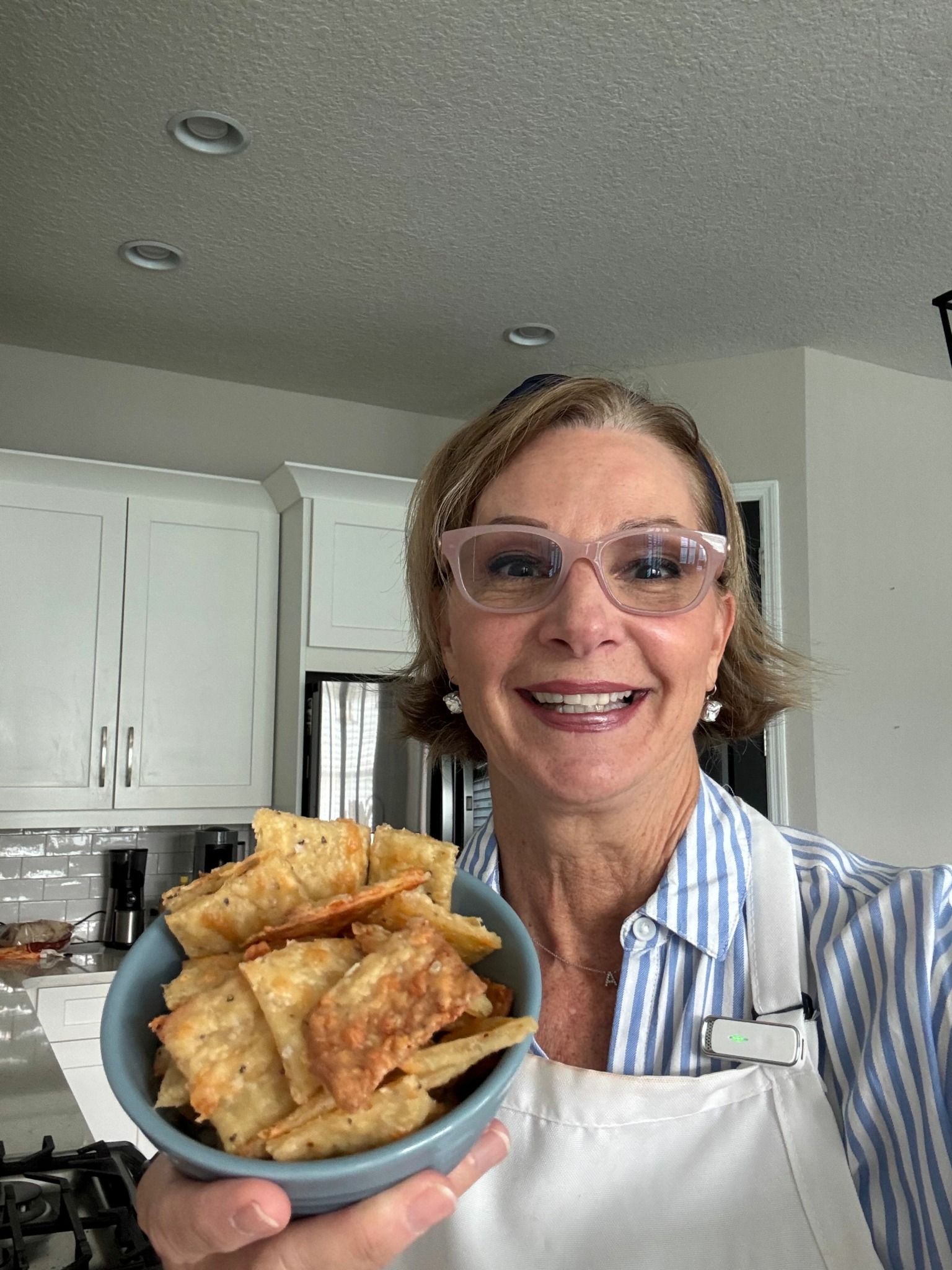 Woman with glasses smiling holding a plate of fried food in a kitchen.