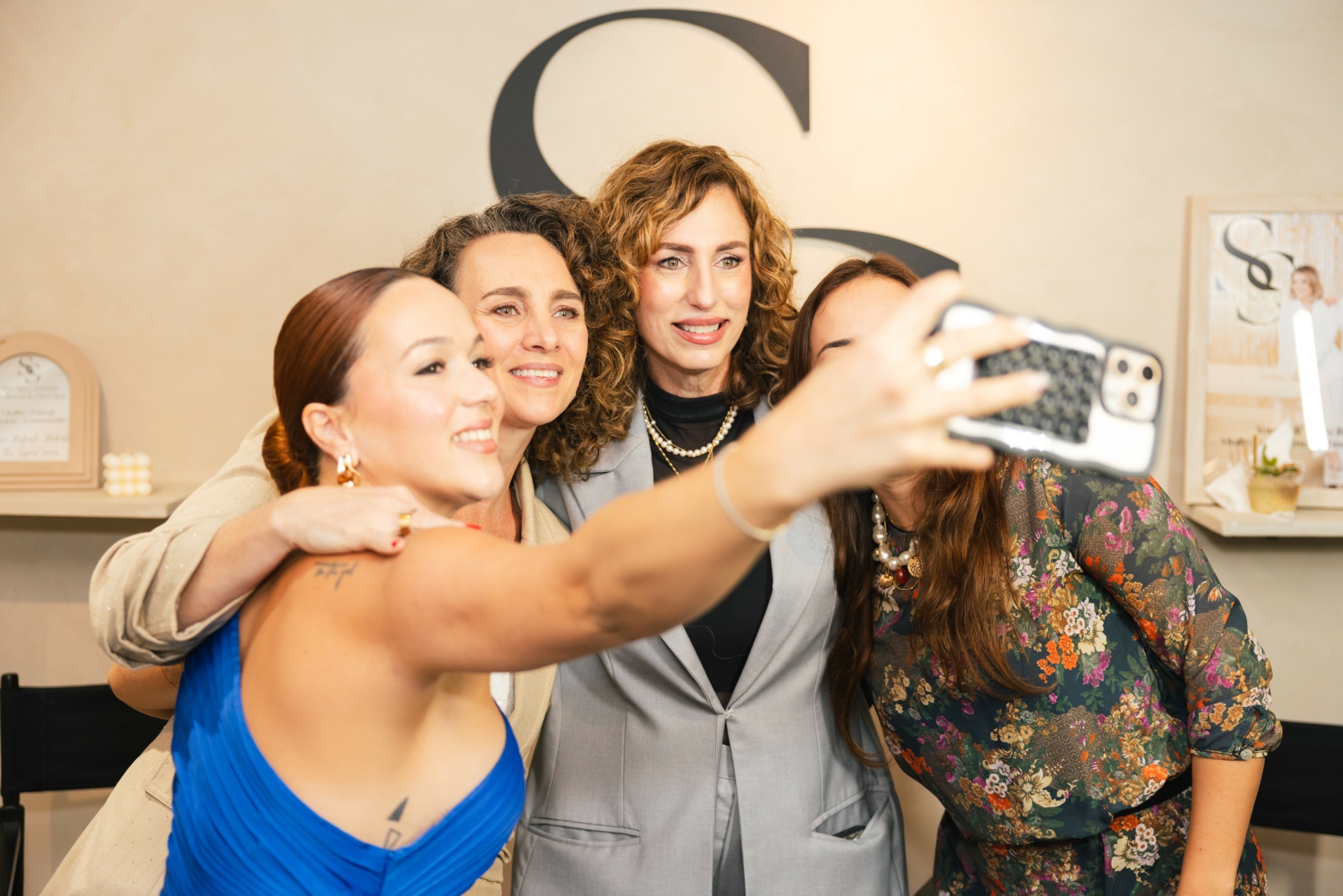 Three women taking a selfie together, smiling, in a room with a large letter 'C' on the wall.