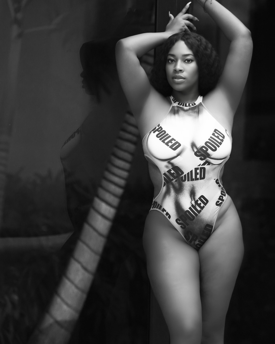 Woman in a swimsuit with police tape pattern, posing with arms above head, in black and white.