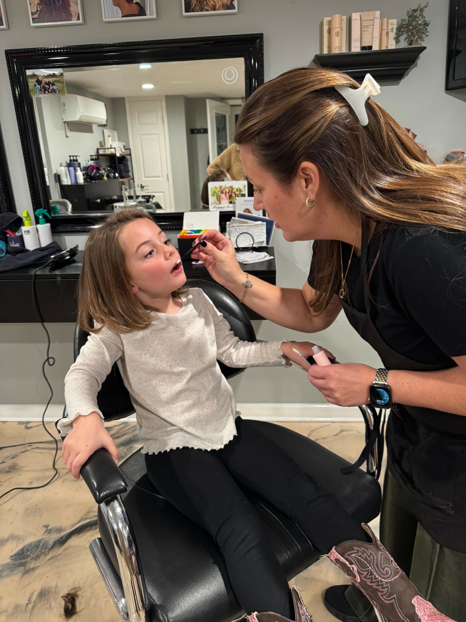 Woman receiving a haircut in a salon, seated in a chair, with hairdresser standing beside her.