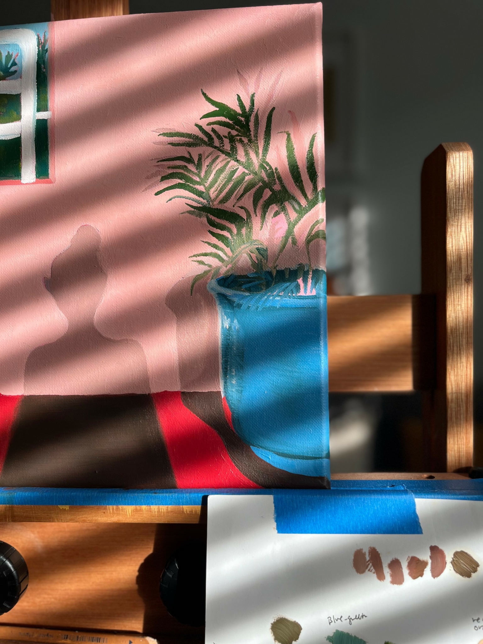 Plant in a blue pot on a wooden chair, with sunlight casting shadows on a pink wall and a white surface.