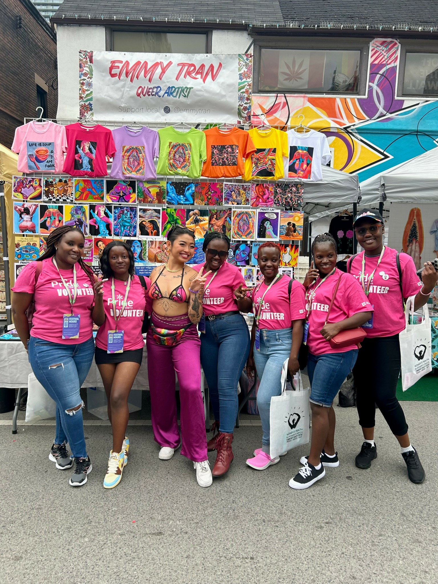 Seven women in pink shirts standing in front of a display of colorful merchandise and a banner reading 'Emmy Tran'.