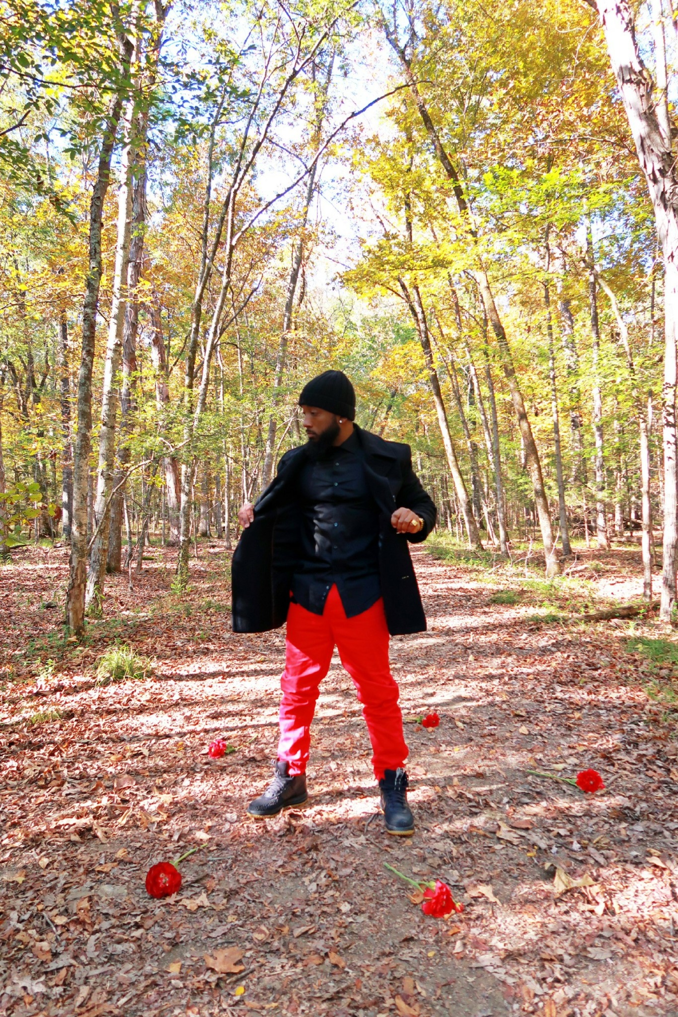 Person standing in a forest with trees and fallen leaves, surrounded by red apples on the ground.
