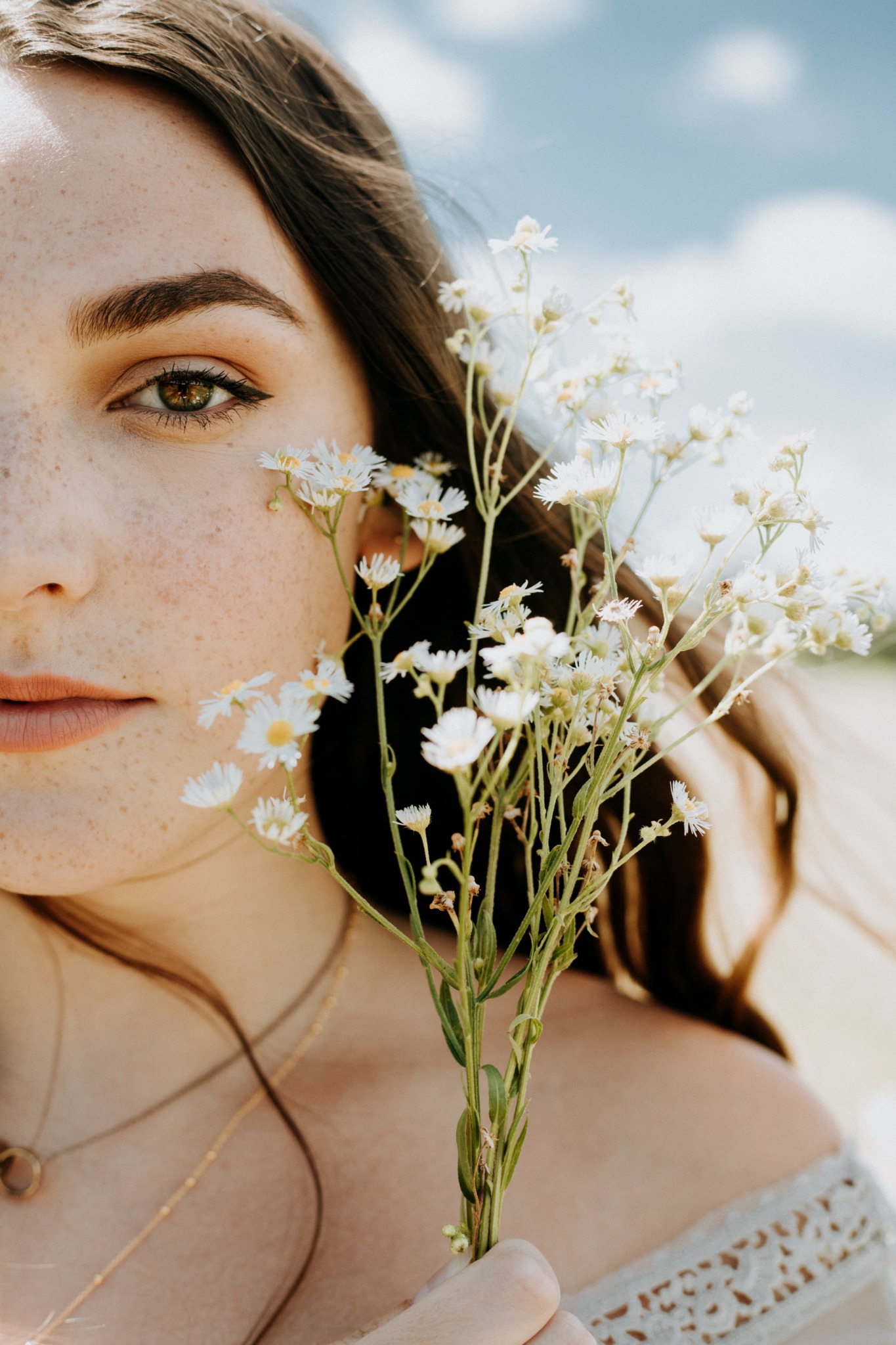 Close-up of a woman holding a bouquet of white flowers outdoors, with a partly cloudy sky in the background.
