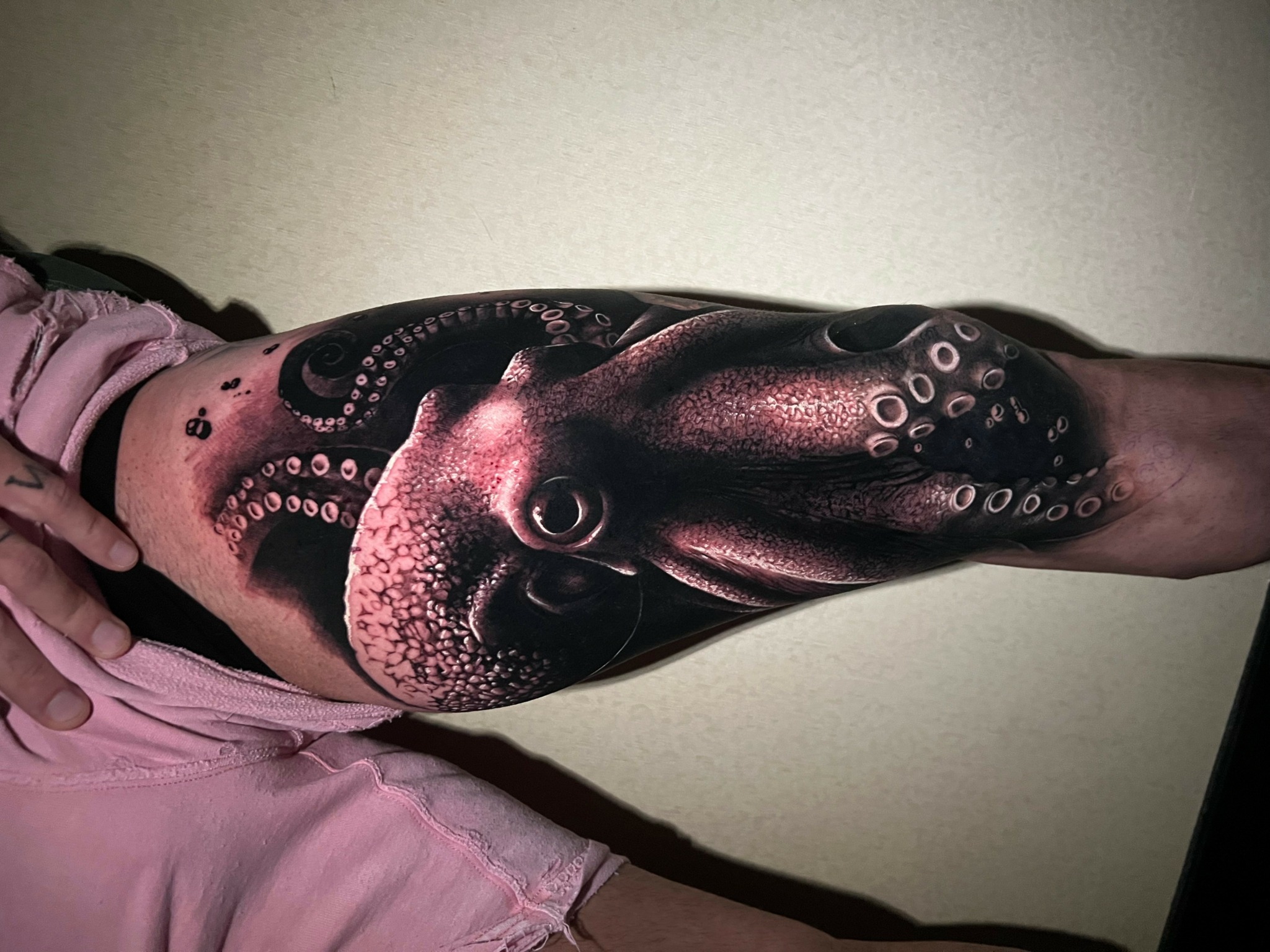 Person with a detailed octopus tattoo on their arm and side, wearing a pink shirt, against a plain background.