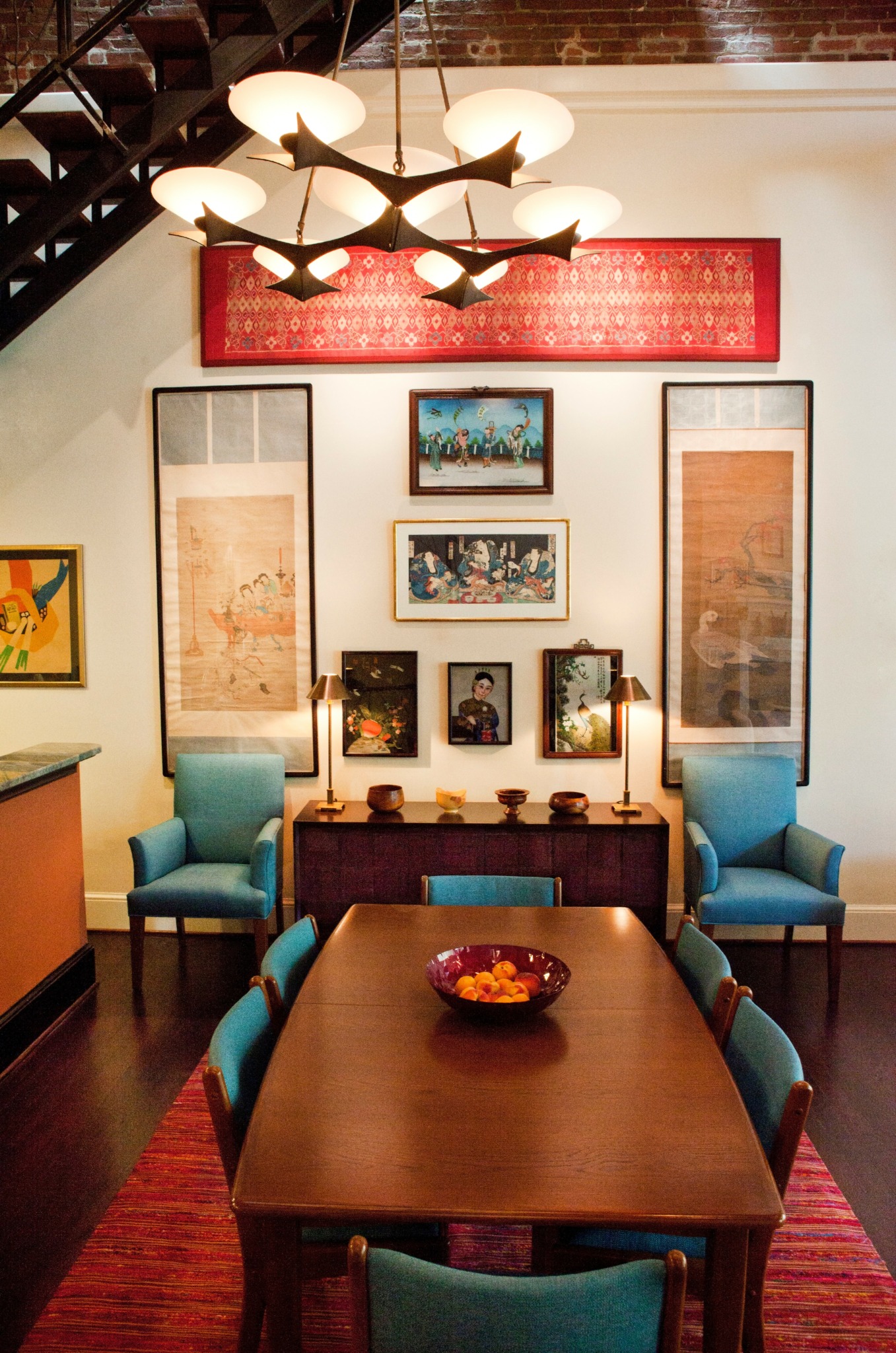 Dining room with wooden table, six chairs, wall art, and a chandelier, with a red rug on the floor.