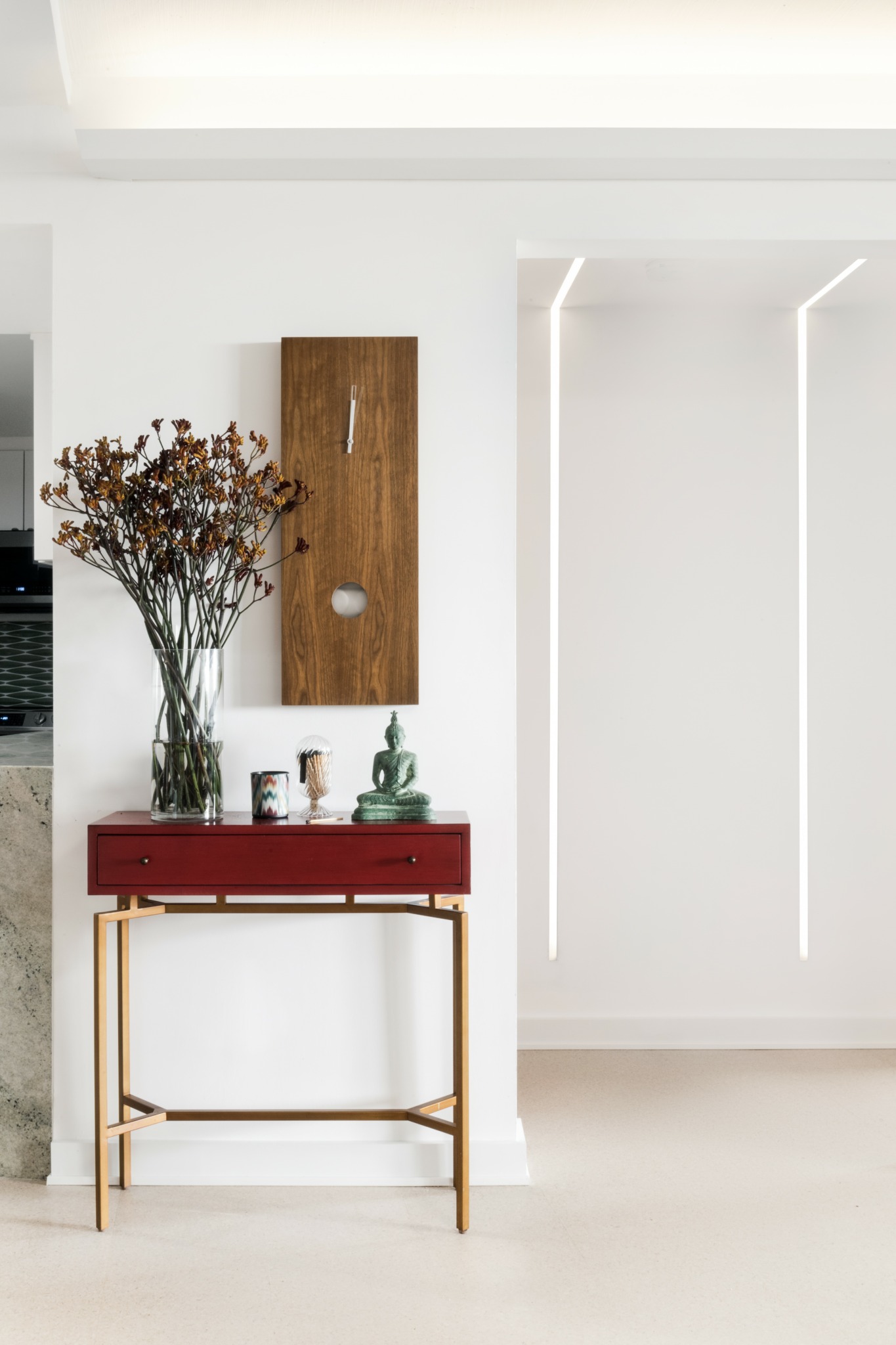 Vase with dried flowers on a red console table against a white wall with a wooden cabinet above.