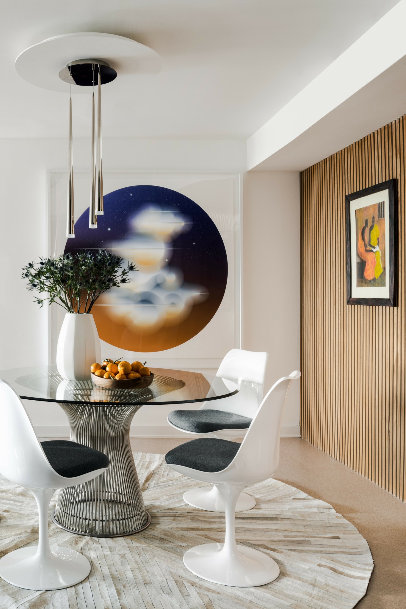 Dining room with round table, four white chairs, large wall art, and a wooden accent wall.
