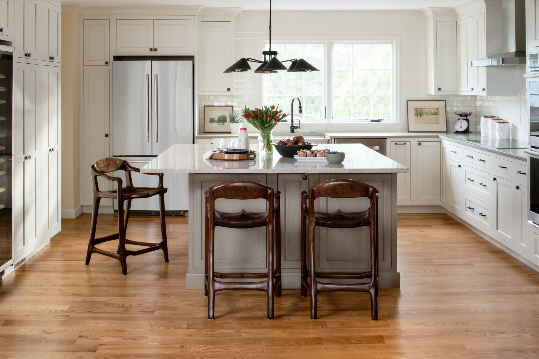 Modern kitchen with white cabinets, a large island with seating, stainless steel appliances, and hardwood floors.
