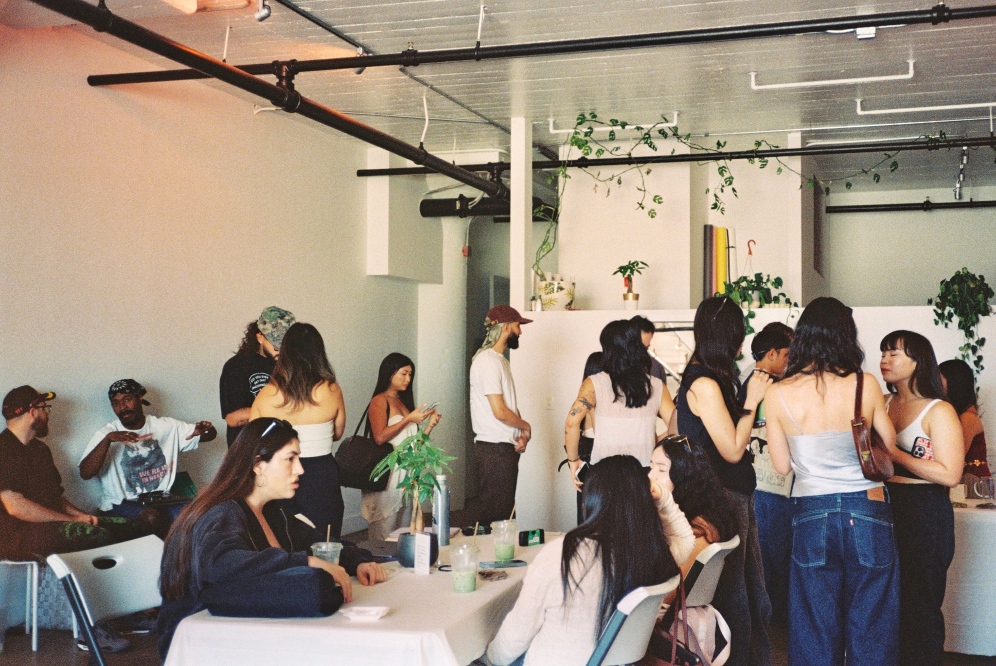 Group of people gathered in a modern indoor space, some sitting at tables, others standing and talking.