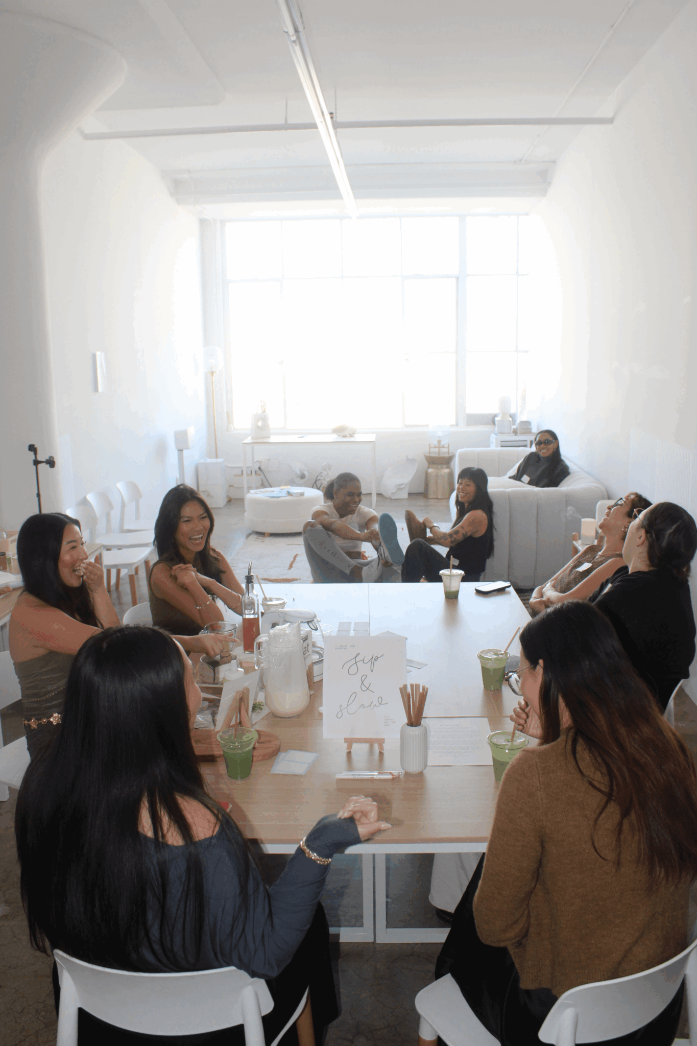 Group of people sitting around a table in a bright room with large windows.
