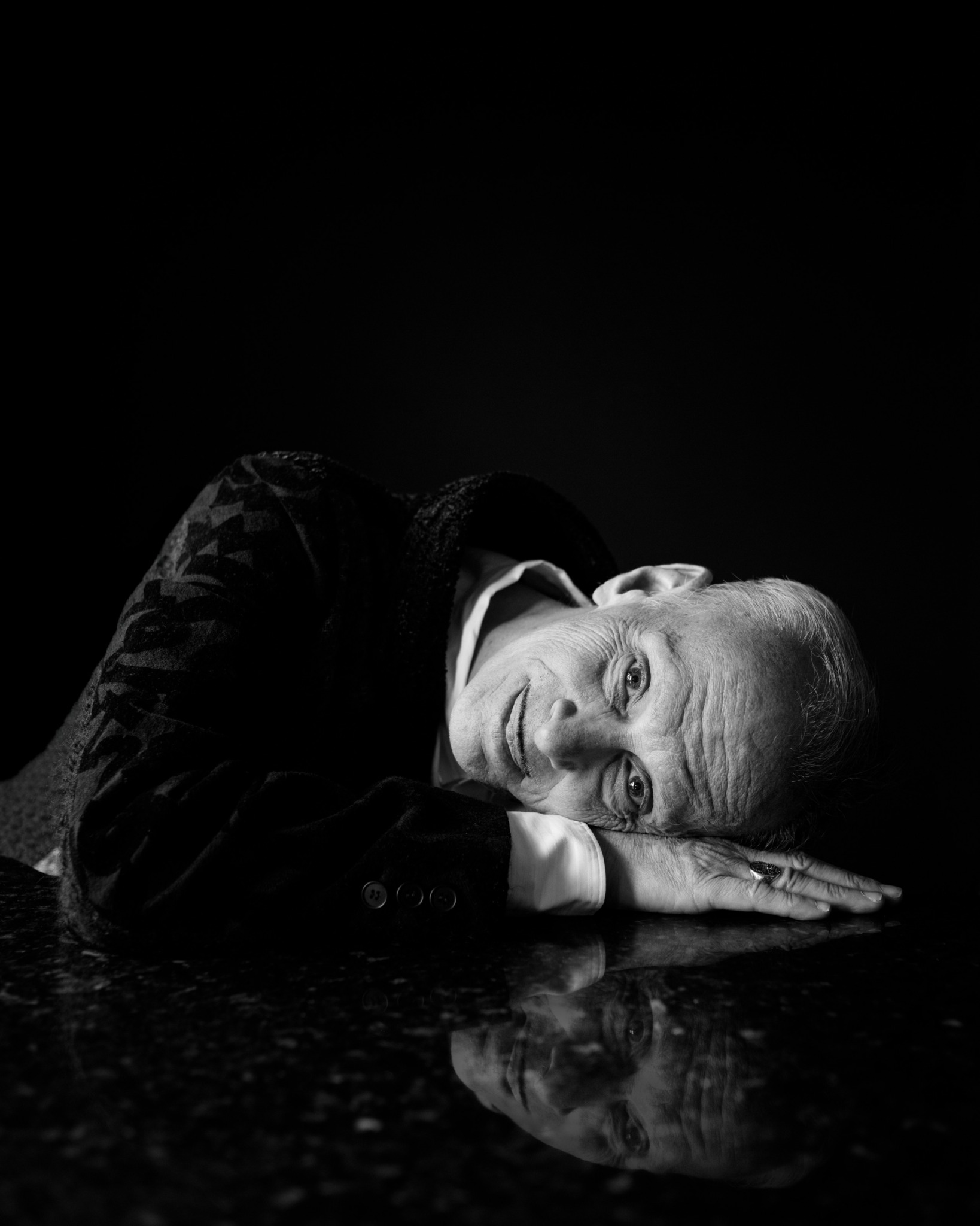 Person lying on their side with head resting on hands, reflected on a shiny surface, in black and white.