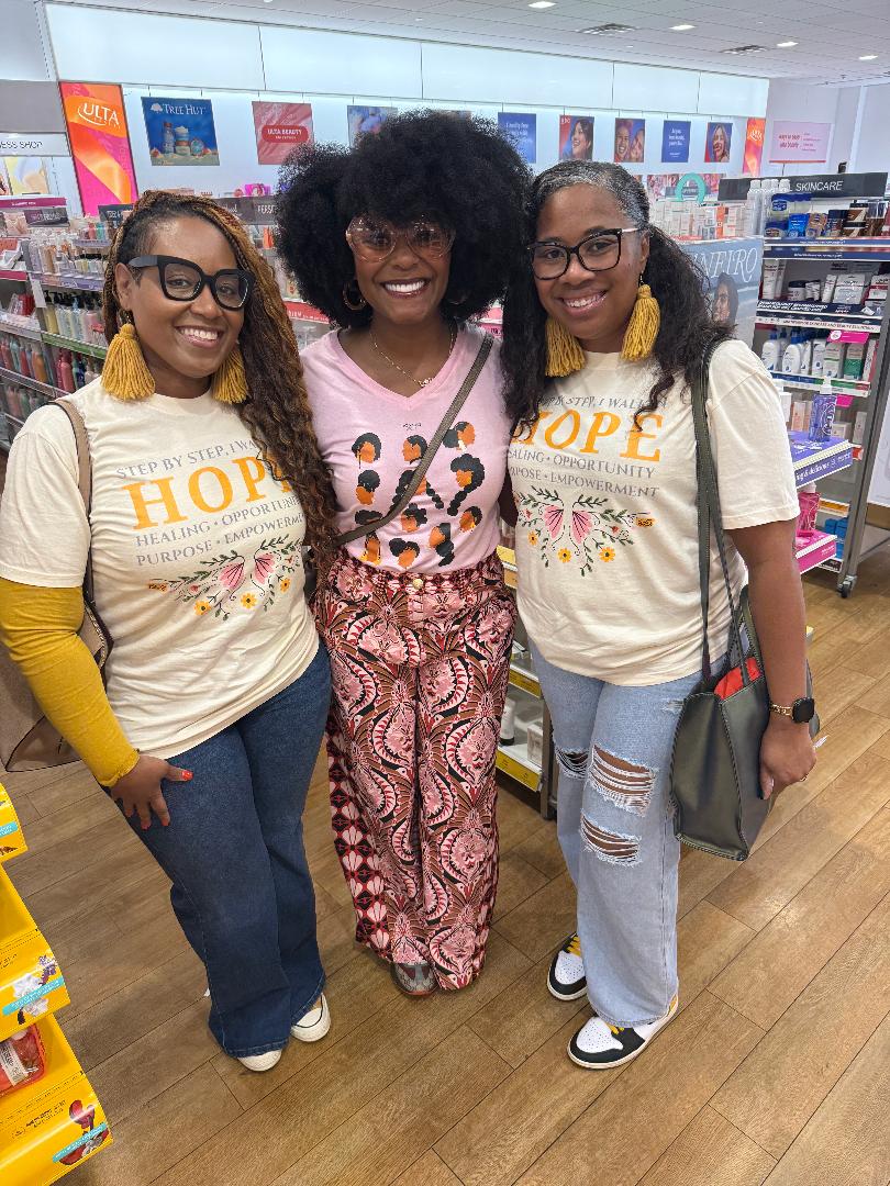 Three women standing together in a store, smiling, with books and shelves in the background.