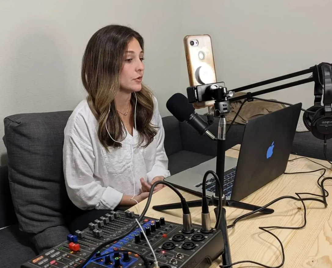 Woman sitting at a desk with a laptop, microphone, and audio equipment, recording or streaming content.