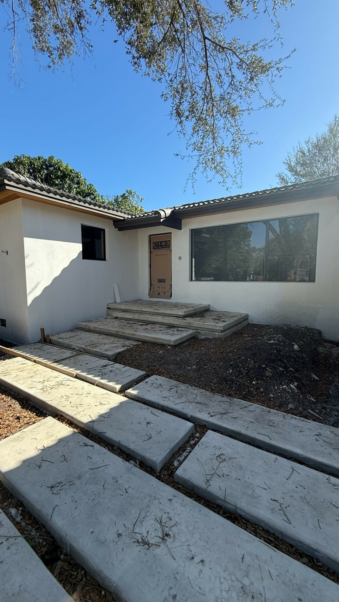 Front view of a house with steps leading to the entrance, large window, and a clear blue sky.