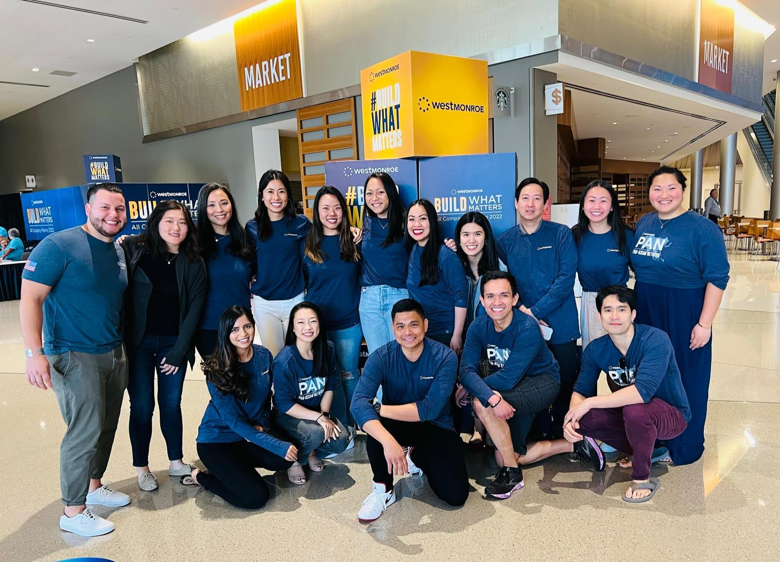 Group of 14 people posing in an indoor shopping mall, some standing and some kneeling, in front of a yellow Westrock sign.