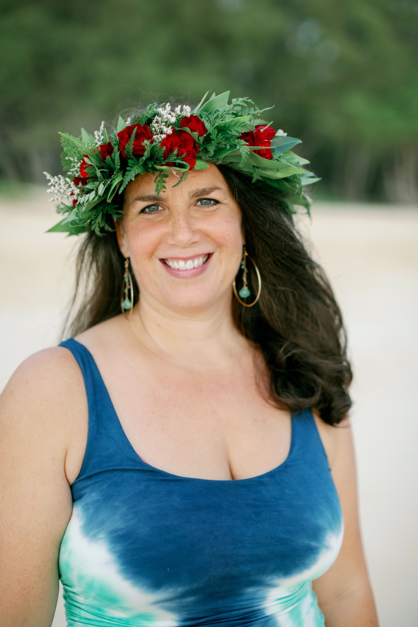 Woman wearing a floral crown and blue dress, smiling outdoors with blurred green background.