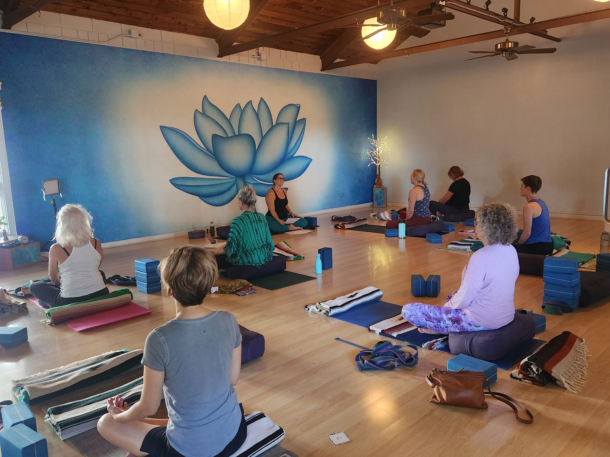 People practicing yoga or meditation in a room with a large lotus flower mural on the wall.