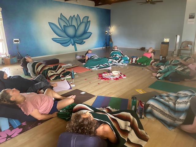 People lying on mats and blankets in a room with a large blue lotus mural on the wall.