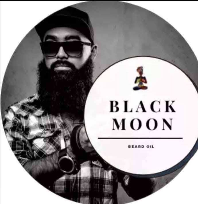 Man with beard, sunglasses, and cap holding a container labeled 'Black Moon Beard Oil'.