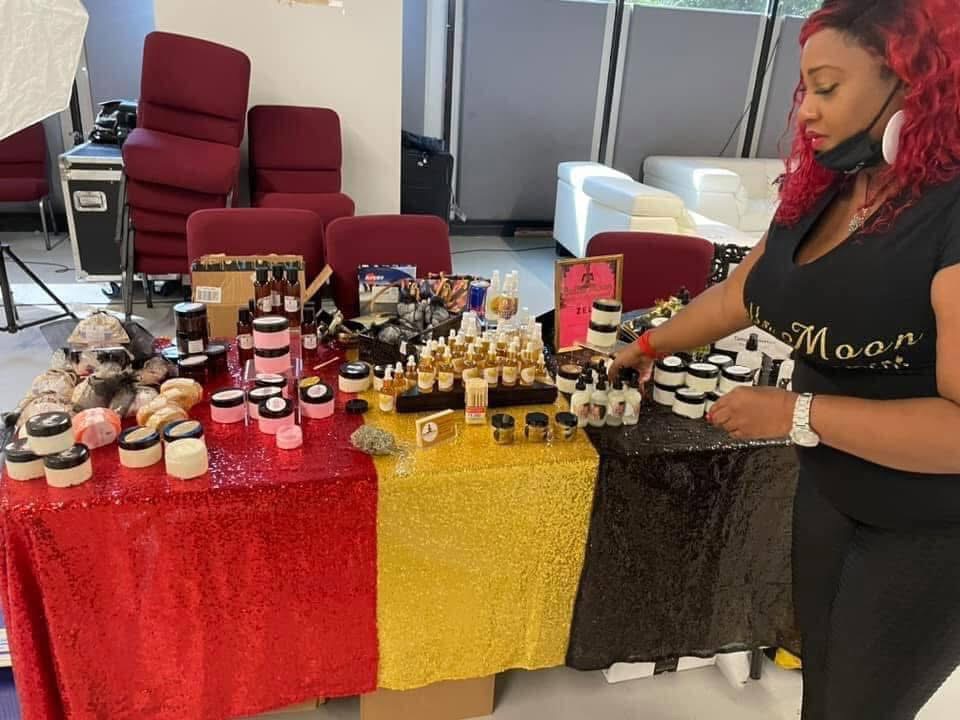 Woman with red hair and headset arranging makeup products on a table with red, yellow, and black cloths.