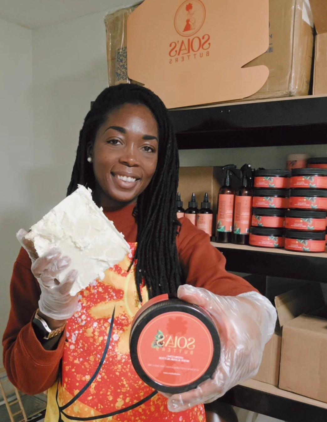 Woman with long dreadlocks wearing gloves, holding a container of Solas product, smiling in a storage room.