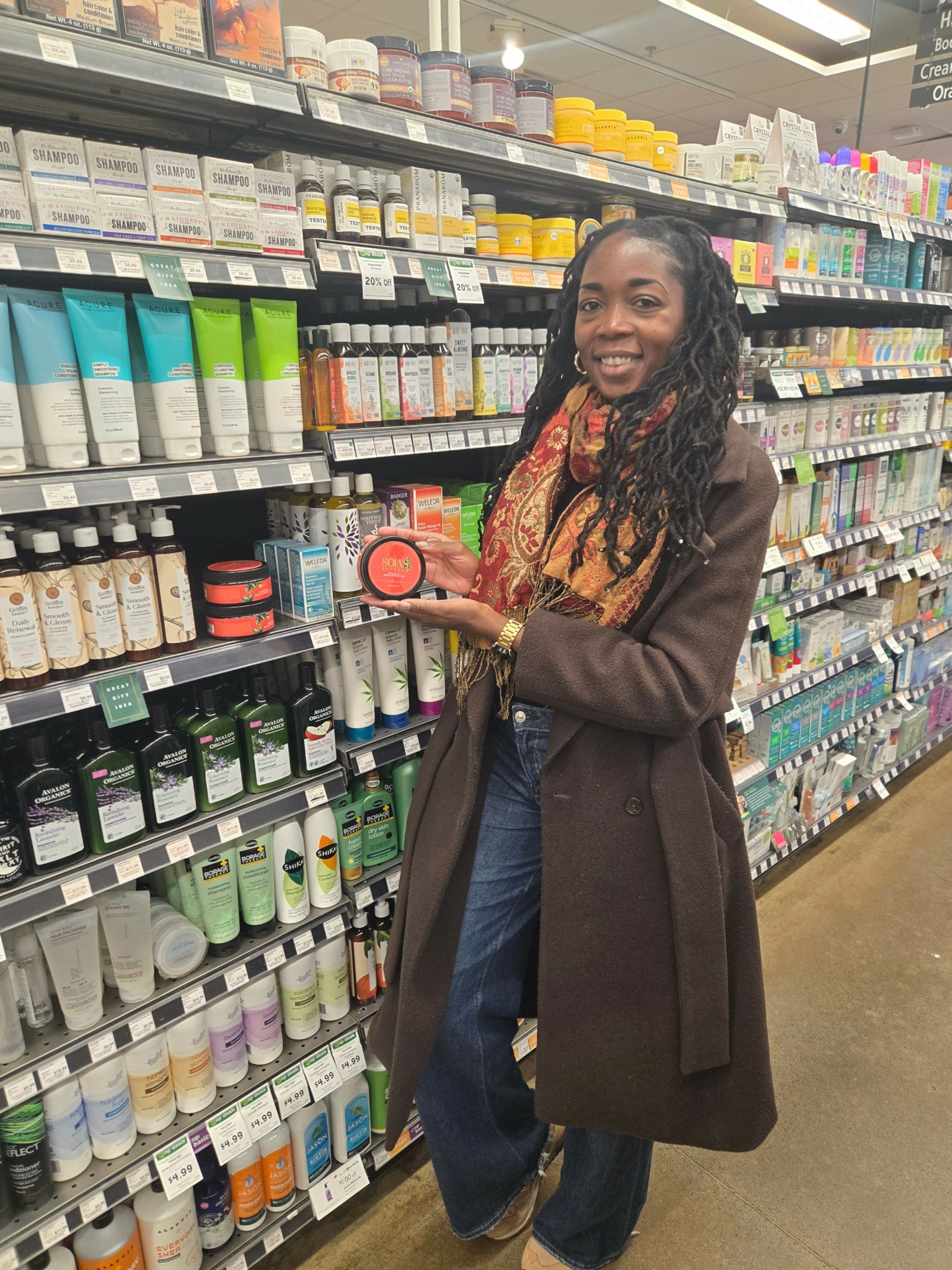 Woman shopping in a pharmacy aisle, holding a red container, surrounded by shelves of medicines and health products.