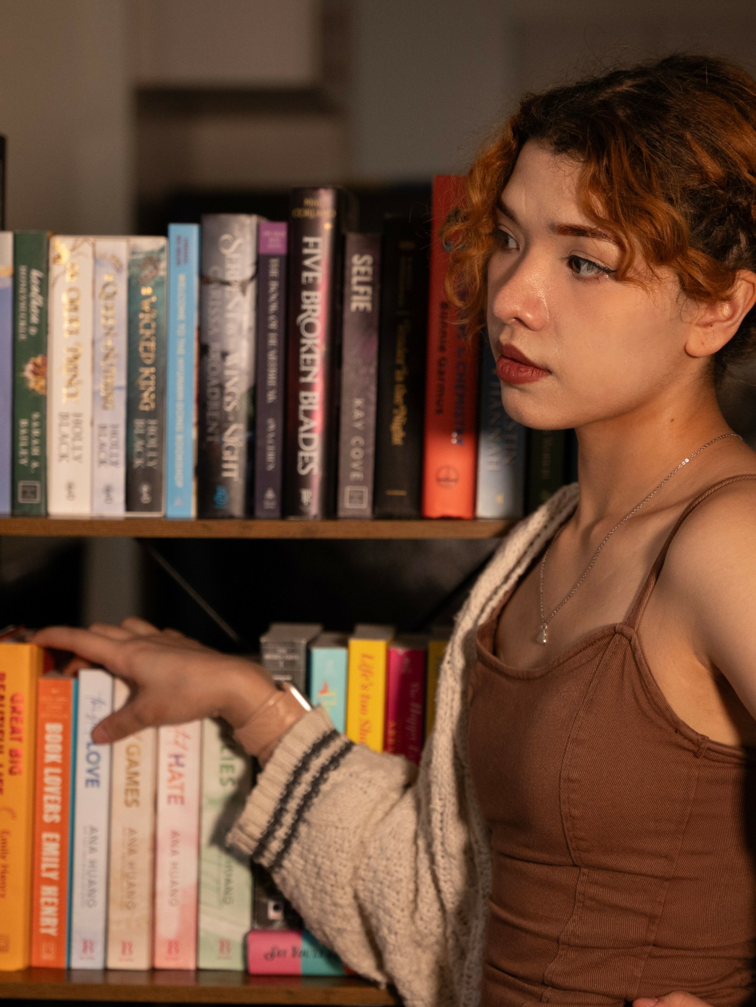 Young woman with curly hair browsing books on a shelf in a library or bookstore.