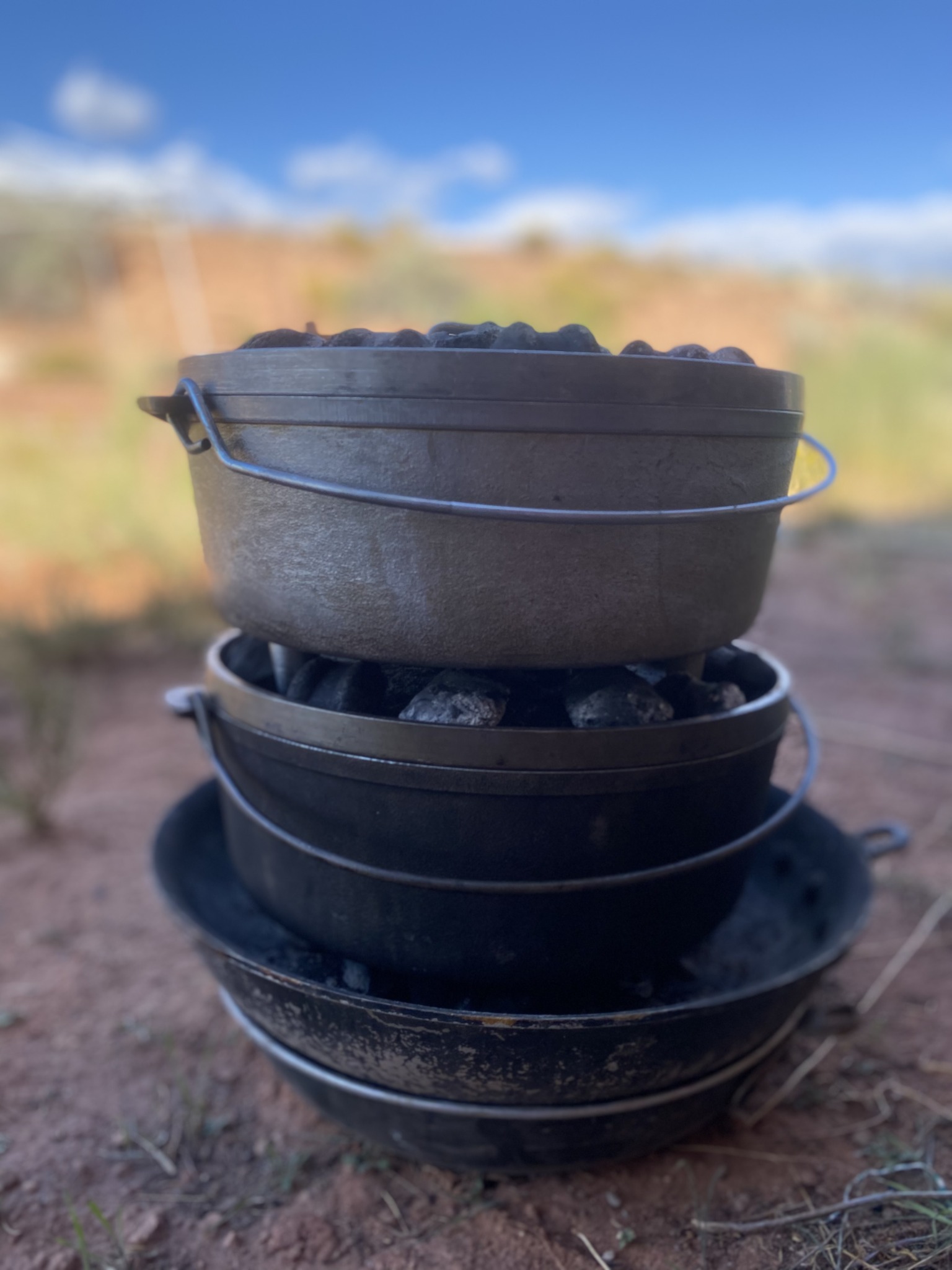 Stacked black and gray pots outdoors with a blurred background of sky and landscape.