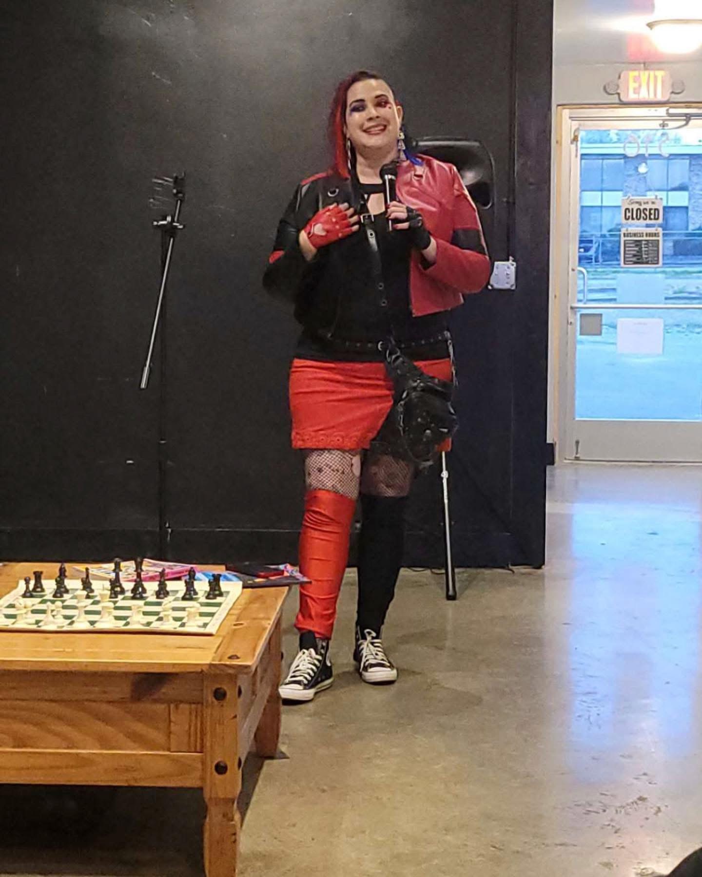 Person with red and black outfit taking a mirror selfie in a room with a chessboard on a wooden table.