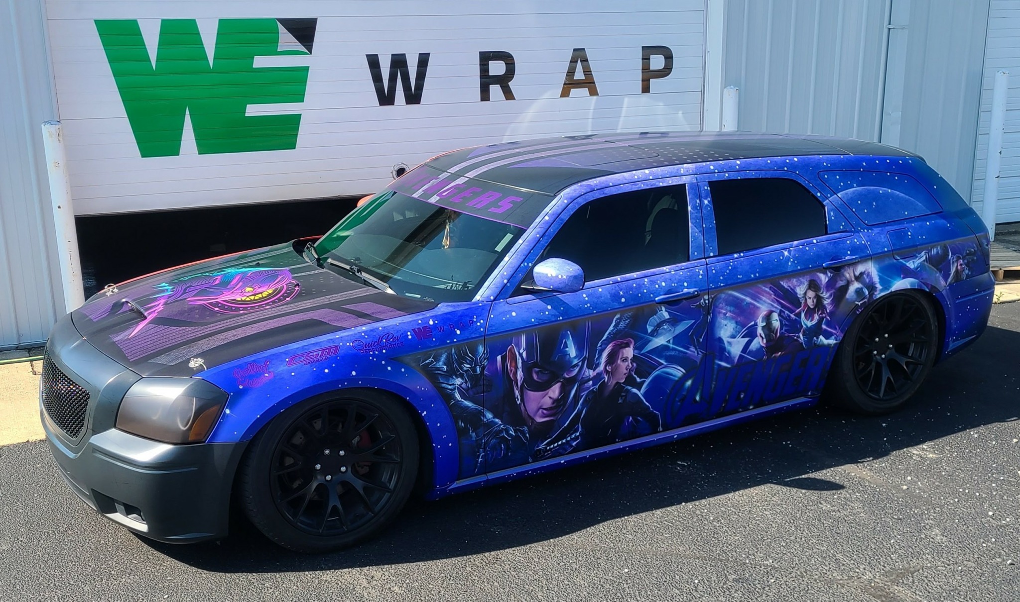 Blue limousine with Marvel superhero artwork parked outside a building with a 'WE WRAP' sign.