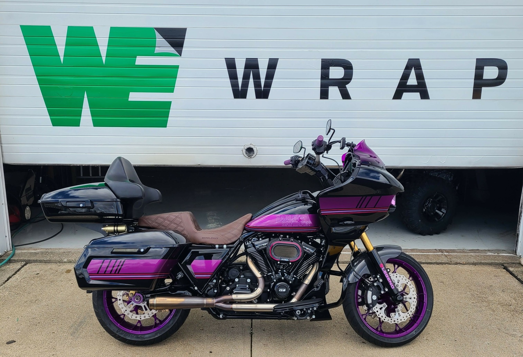 Purple motorcycle with black and gold accents parked in front of a white wall with green and black text.