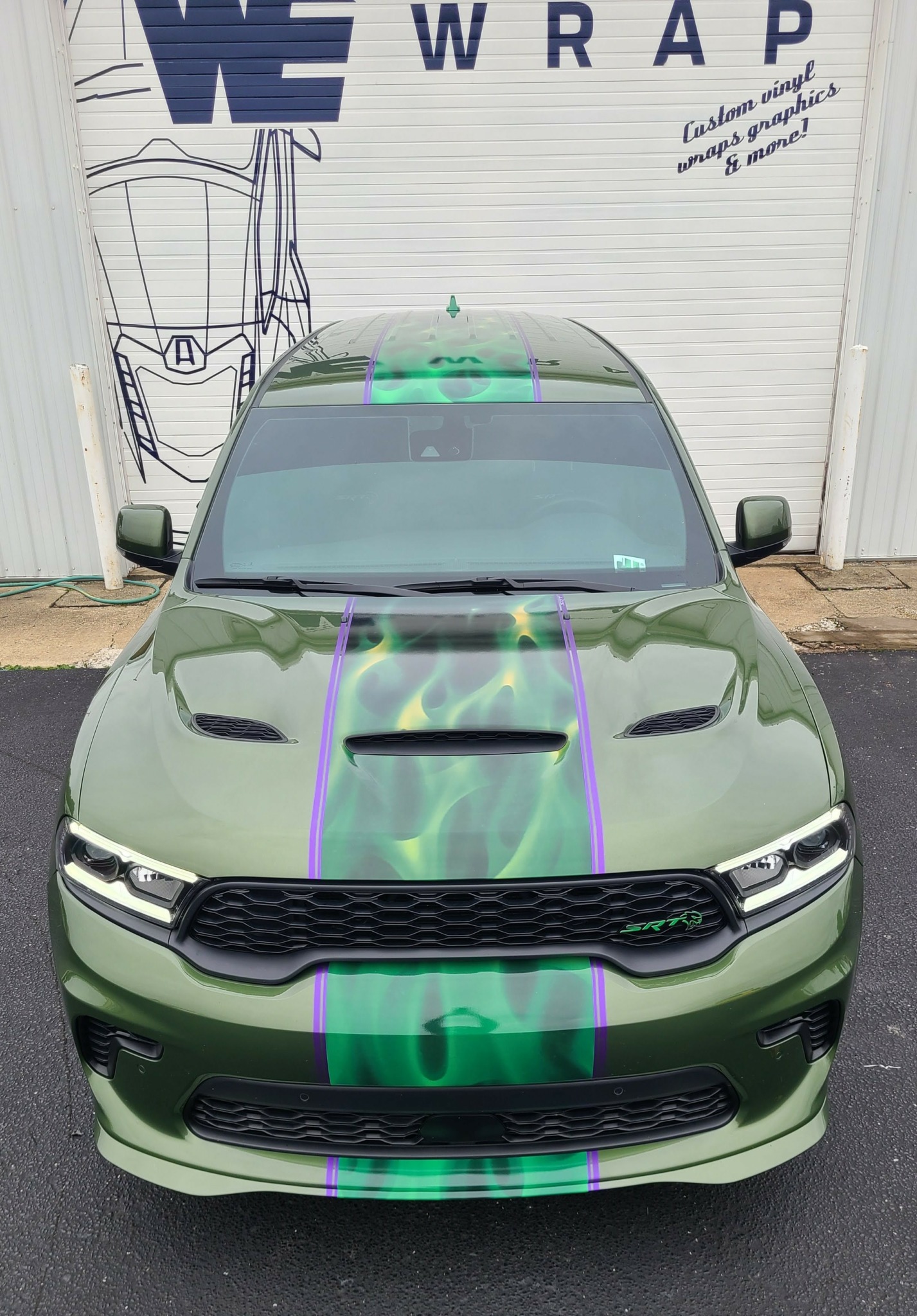 Front view of a green car parked outdoors, with a white background and some text and drawings on the wall.