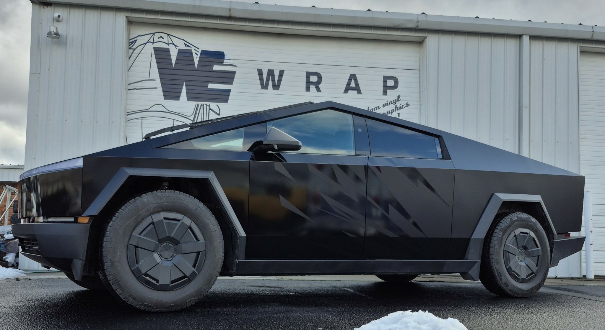 Black futuristic car parked in front of a building with a sign reading 'WRAP'.