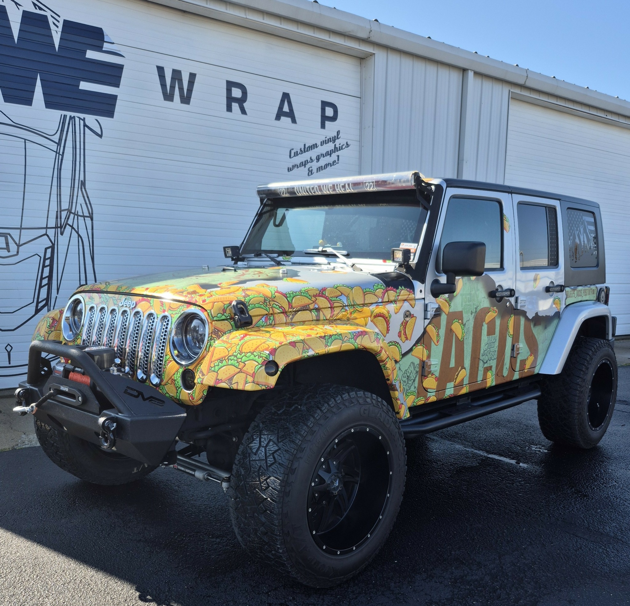 Jeep with colorful, abstract wrap parked outside a building with a sign reading 'WRAP'.