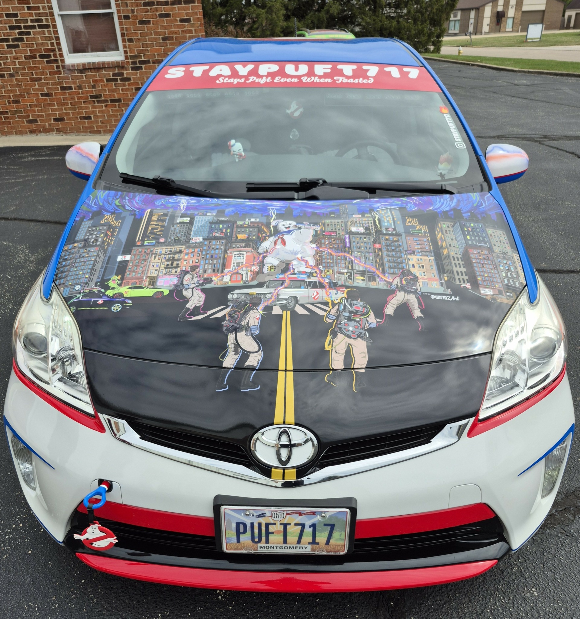 Front view of a decorated car with cityscape graphic, yellow road line, and a red banner on top.