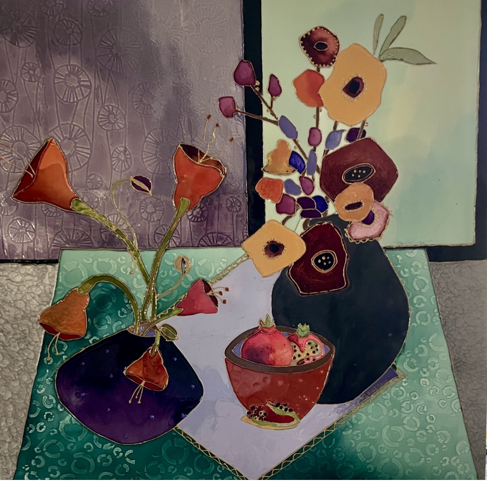 Two vases with colorful paper flowers on a table with a patterned cloth, background with textured wall and artwork.