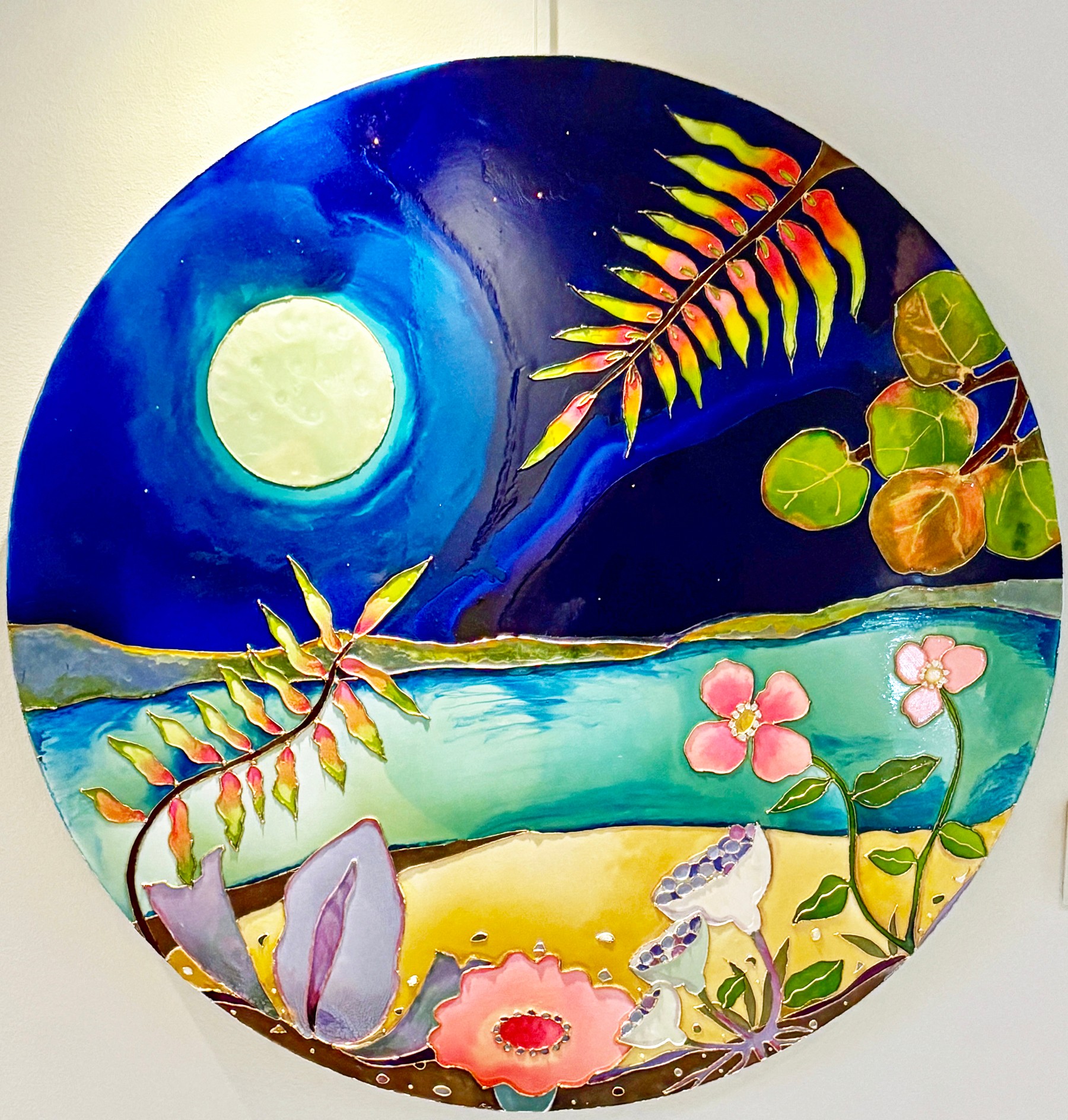 Colorful circular painting of a landscape with a moon, trees, flowers, and water scene.