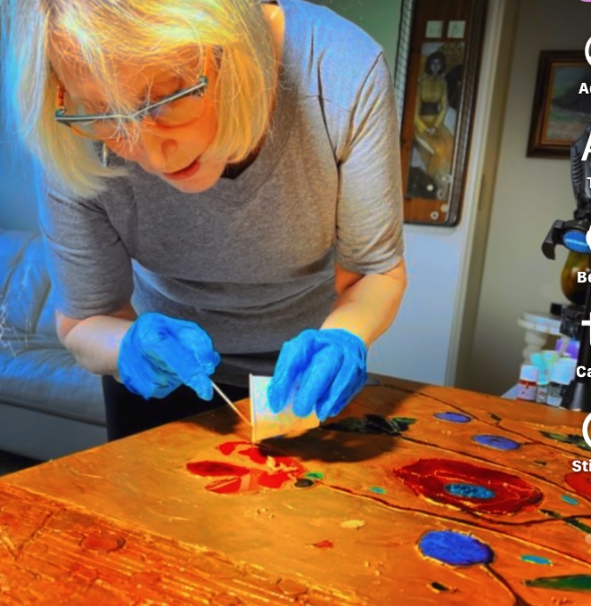 Person with orange hair, glasses, and blue gloves painting on a wooden surface.