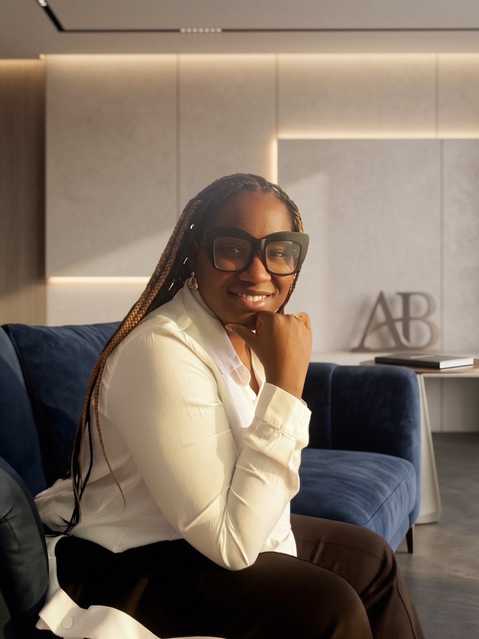 Woman with glasses smiling, sitting on a blue sofa in a modern room with light-colored walls.