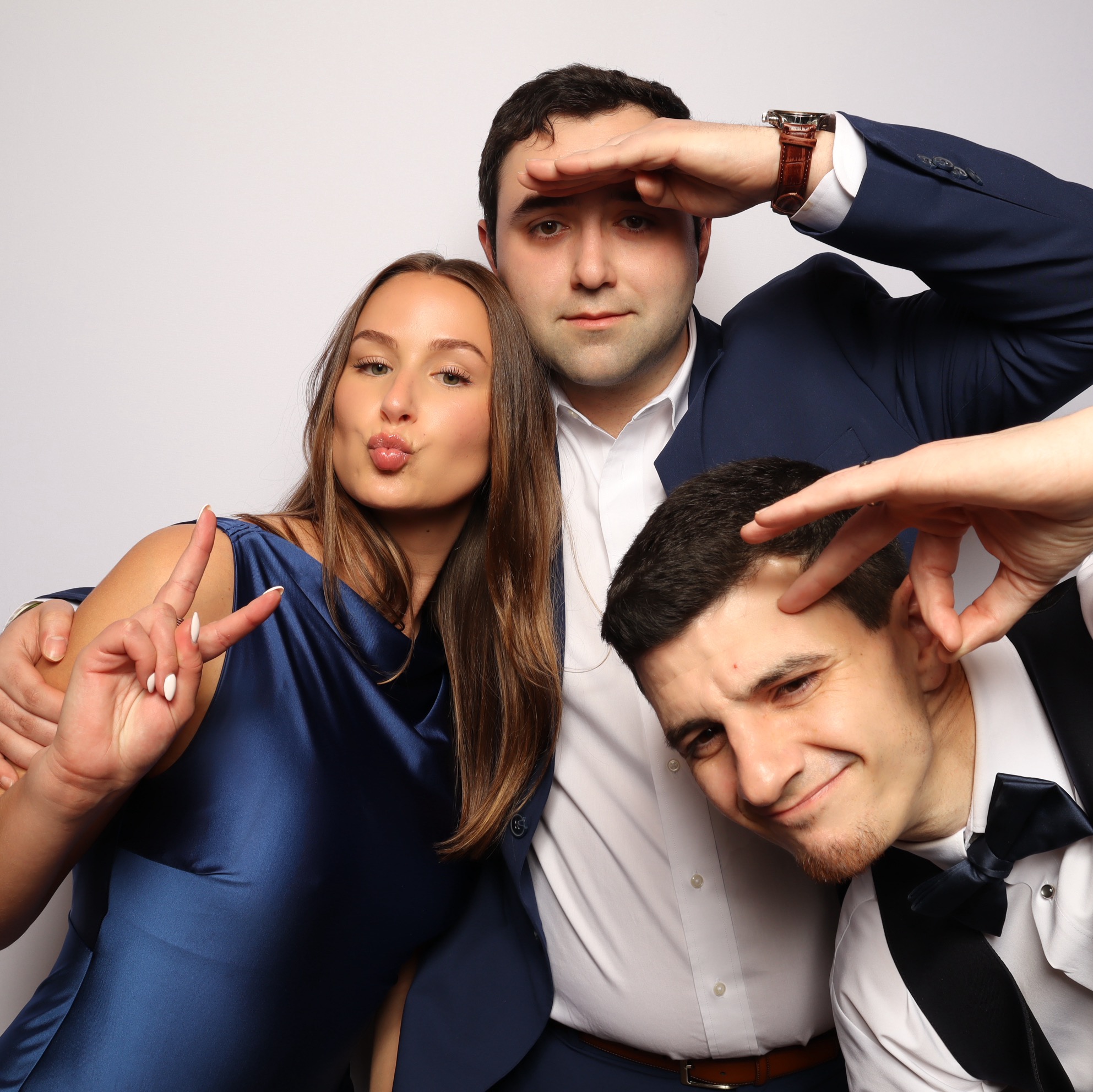 Three people posing together, one woman and two men, making playful gestures and expressions.