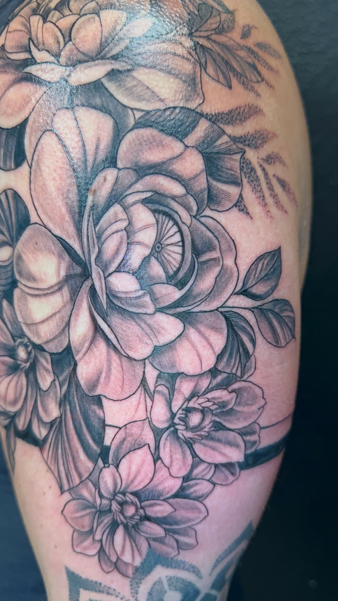 Black and gray floral tattoo with roses and leaves on person's arm.