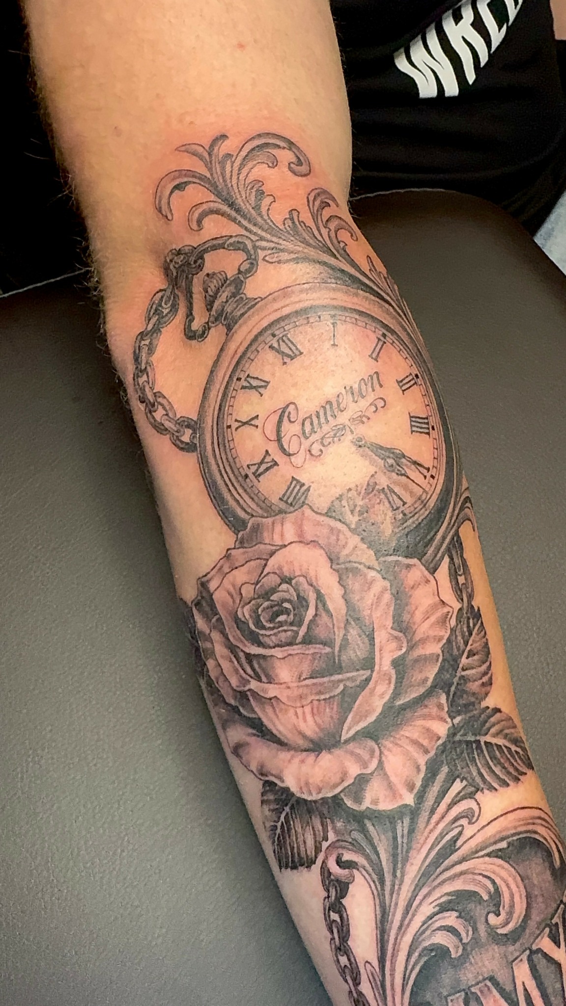 Tattoo of a pocket watch with Roman numerals and a rose below it on a person's forearm.