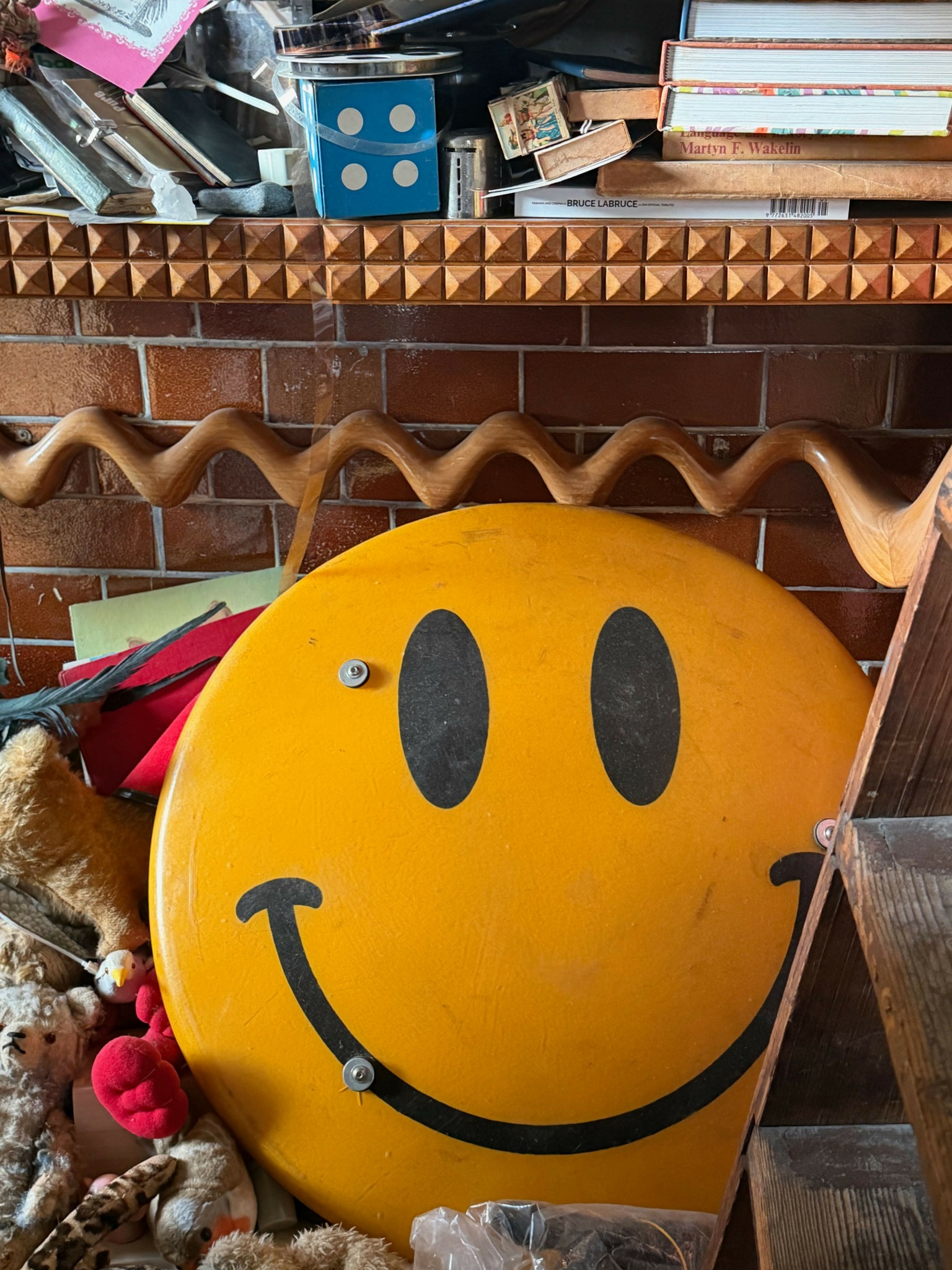 Yellow smiley face sign with black eyes and a curved smile, leaning against a wooden surface.